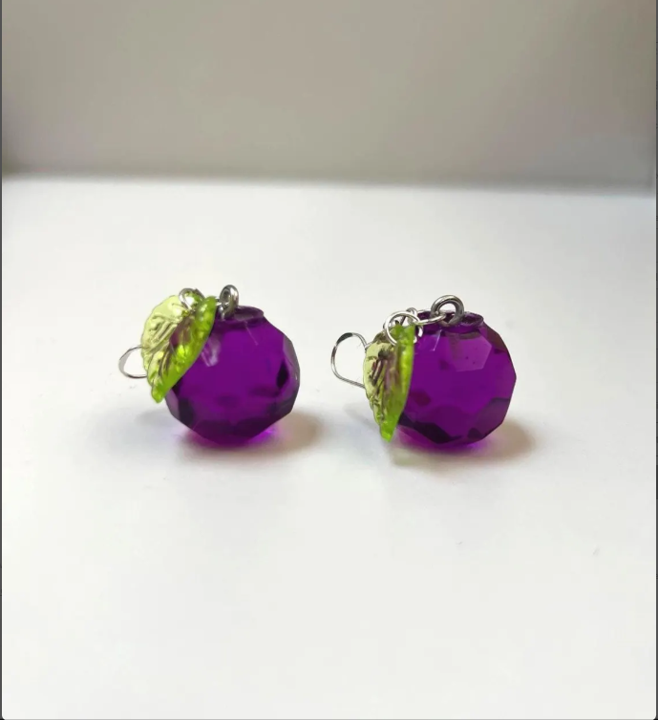 Purple multifaced earrings with green leaves on a white background
